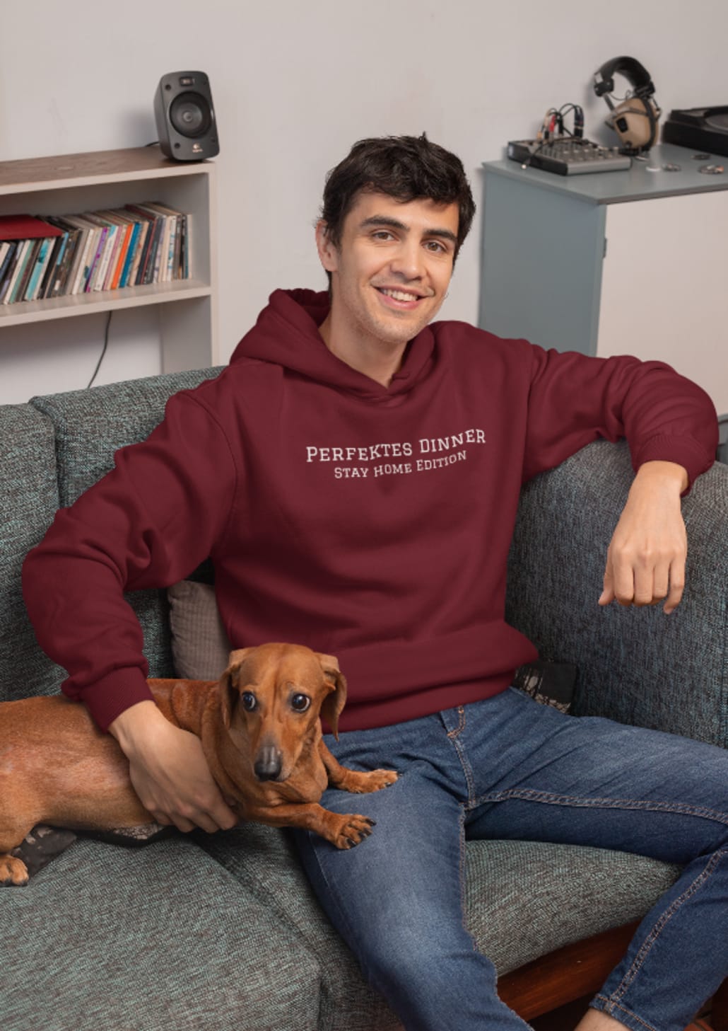 junger Mann mit rotem Hoodie sitzt auf Couch mit süßen Hund